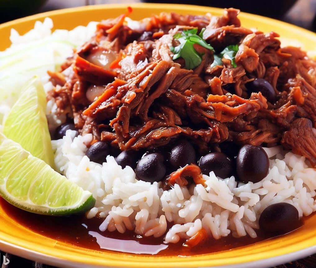Ropa vieja, Cuban shredded beef in tomato sauce, over white rice with black beans and a lime wedge on a yellow plate
