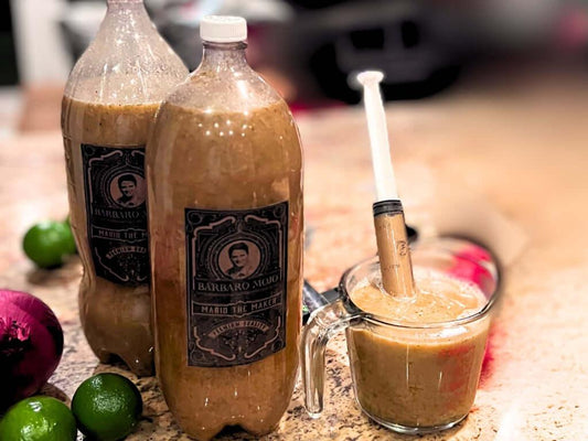 Two bottles of Barbaro Mojo criollo marinade with a measuring cup of the citrus-garlic marinade and limes on a kitchen counter