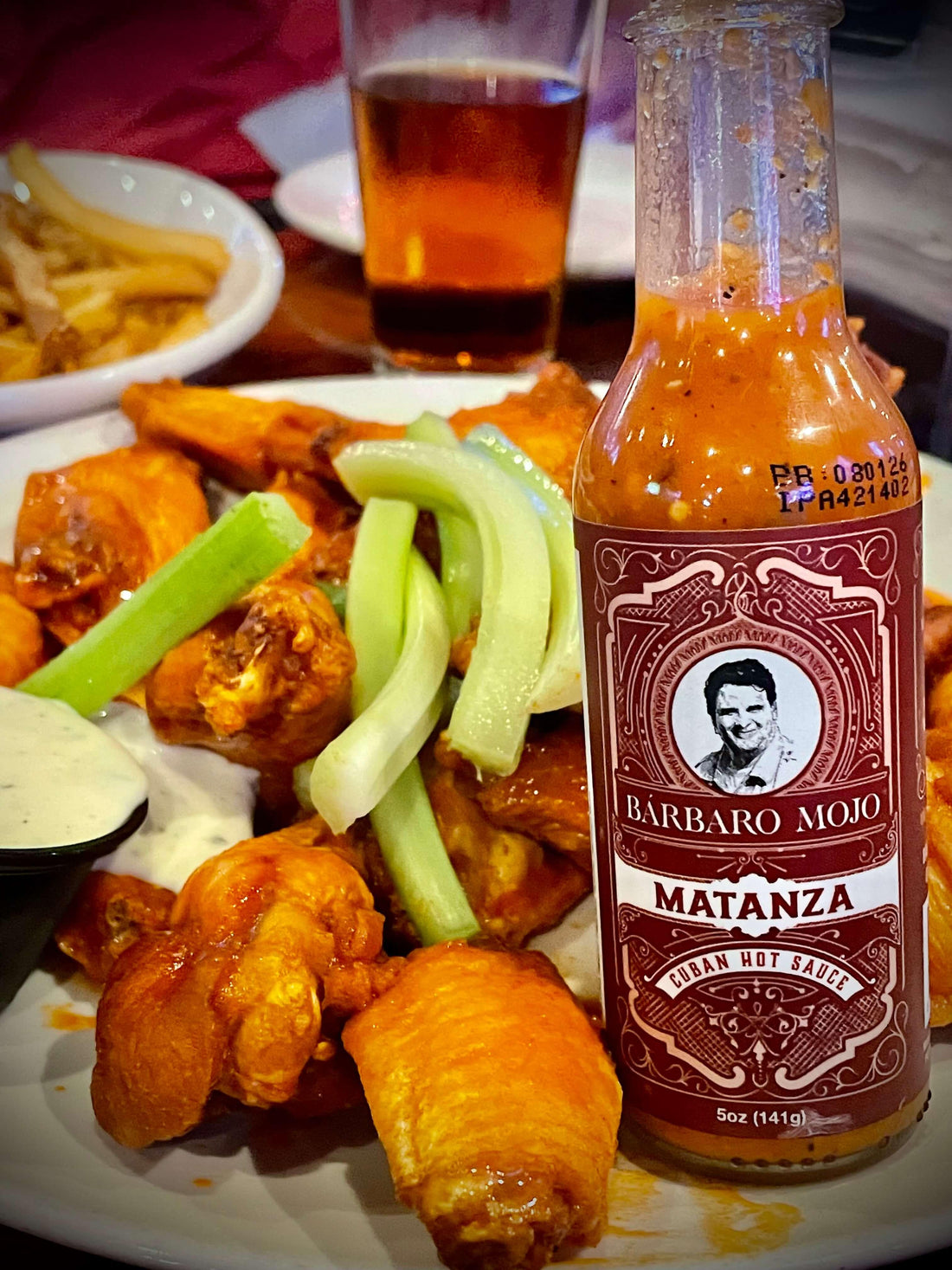 Bottle of Barbaro Mojo Matanza hot sauce beside a plate of chicken wings and celery sticks