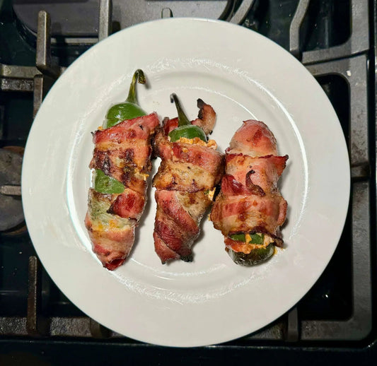 Three bacon-wrapped jalapeño poppers on a white plate, fresh from the oven