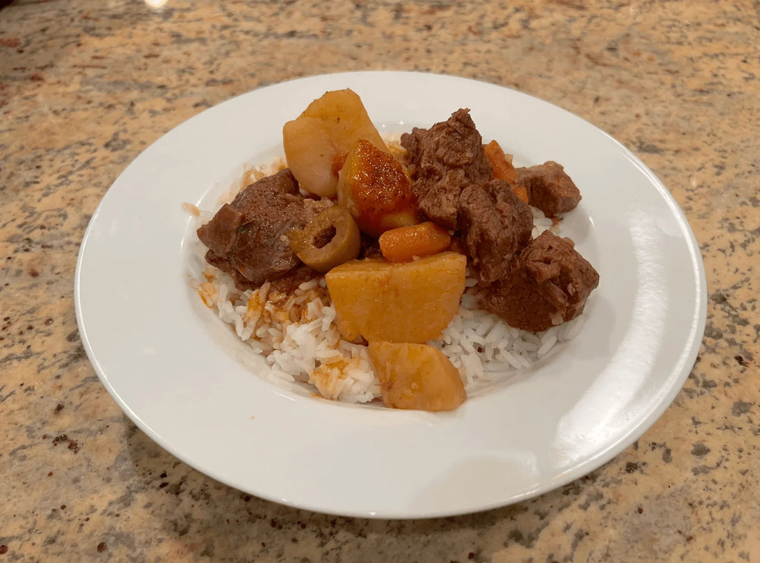 Carne con papas, Cuban beef and potato stew with olives, served over white rice on a white plate