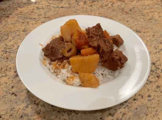 Carne con papas, Cuban beef and potato stew with olives, served over white rice on a white plate