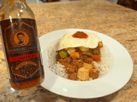 Cuban picadillo a caballo, ground beef with green olives over white rice topped with a fried egg, beside a bottle of Barbaro Mojo El Havanero
